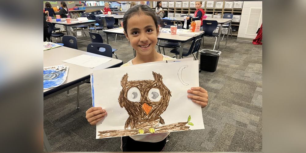 A students holds their artwork of an owl.