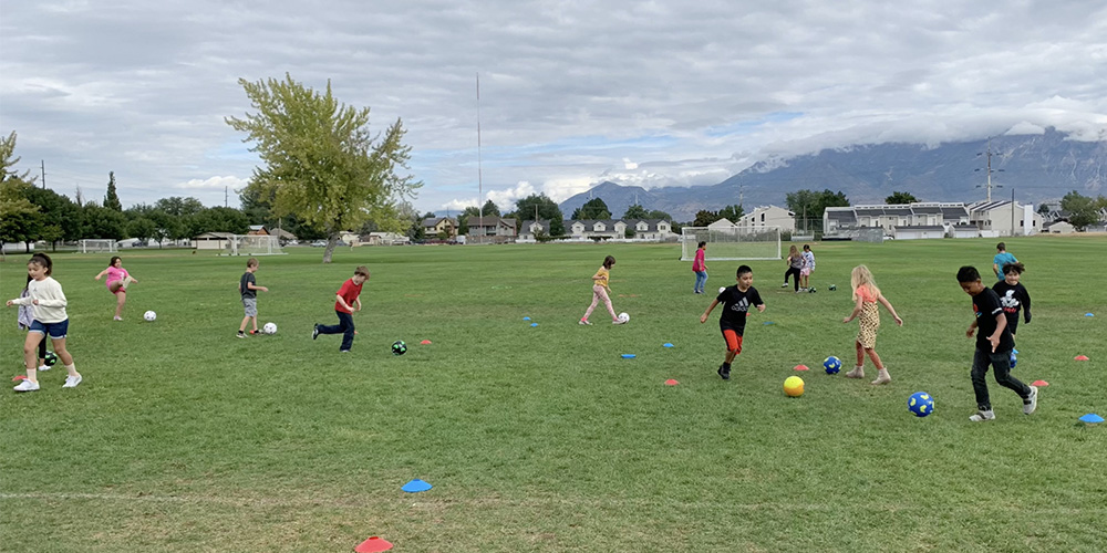 Students kick a ball between cones on the field